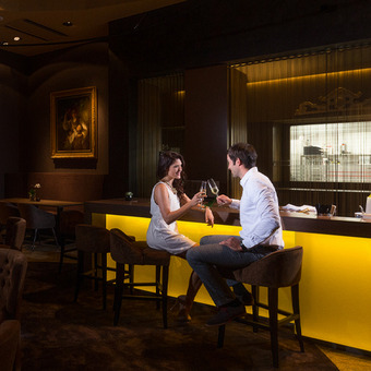Stilvoll gekleidetes Pärchen stößt mit zwei Champagnergläsern an der Hotelbar an